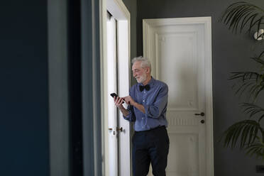 Älterer Mann telefoniert zu Hause am Fenster stehend - EIF00616