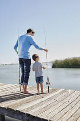 Father and son holding fishing rod while standing on pier - RORF02669