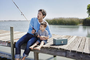 Älterer Mann und Junge fischen zusammen, während sie auf dem Pier sitzen - RORF02675