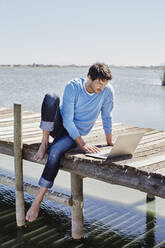 Mature man using laptop while sitting on pier - RORF02686