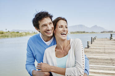 Cheerful woman sitting with smiling man on pier - RORF02687