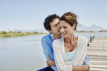 Mature man kissing while embracing woman on pier - RORF02689