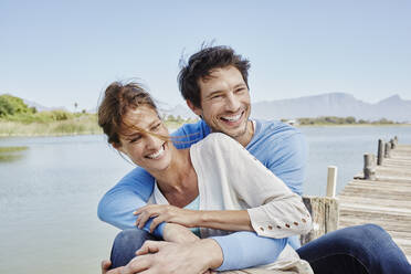 Happy couple sitting together on pier - RORF02690