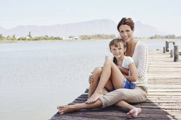 Smiling mother and boy sitting on pier during sunny day - RORF02694