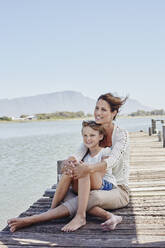 Smiling boy sitting with mother on pier - RORF02695