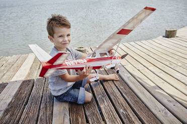 Lächelnd niedlichen Jungen spielen mit Flugzeug Spielzeug auf Pier - RORF02703