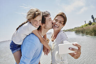 Cheerful family taking selfie through mobile phone by lake - RORF02707