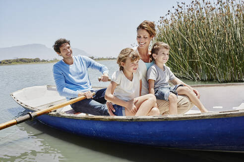 Mature man paddling while sitting with family in rowboat on sunny day - RORF02708