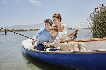 Parents with fishing rod sitting by son in rowboat on lake - RORF02709