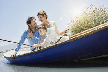 Son fishing while sitting by parents in rowboat during sunny day - RORF02710