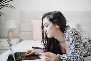 Frau mit Kreditkarte beim Online-Shopping mit Laptop auf dem Bett - EBBF02612