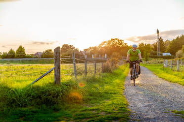Mann fährt Mountainbike auf einem Feldweg - CUF57878