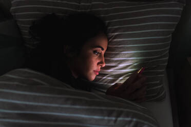 Young woman lying in bed and looking at phone - CUF57896