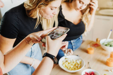 Frau fotografiert mit dem Handy, während Freunde Eigentum freigegeben (PR) Essen zubereiten - CUF57919