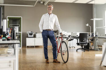 Male entrepreneur with bicycle standing in open plan office - PESF02640