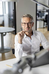 Male entrepreneur holding pen while sitting at desk in office - PESF02647