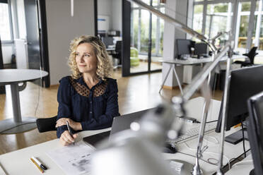 Businesswoman looking away while sitting at desk in office - PESF02655