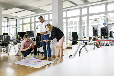 Businesswoman by colleagues photographing business plan in open plan office - PESF02664