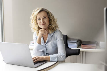 Beautiful businesswoman with hand on chin sitting in office - PESF02684