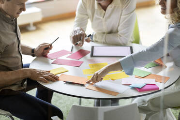 Unternehmerin, die auf ein Papier zeigt, während sie mit einem Kollegen an einem Tisch im Büro sitzt - PESF02693