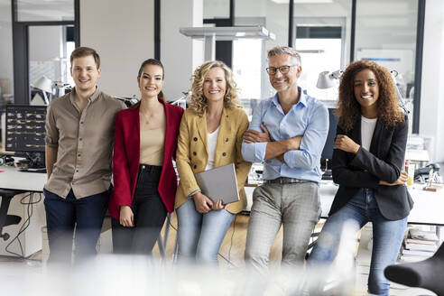 Smiling male and female colleagues leaning at desk in office - PESF02714