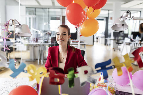 Beautiful smiling female entrepreneur sitting in office during birthday celebration - PESF02722