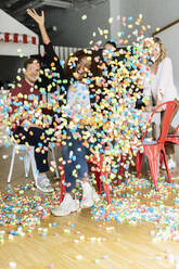 Cheerful businesswoman with arms raised sitting amidst playmais against colleagues in office - PESF02741