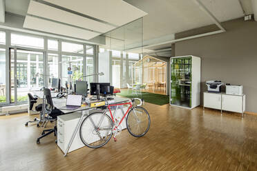 Bicycle, laptop and computers at desk in open plan office - PESF02749