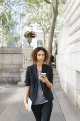 Afro-Geschäftsfrau benutzt Smartphone beim Gehen auf dem Fußweg - BOYF01937