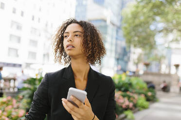 Thoughtful Afro female entrepreneur with smart phone in city - BOYF01940