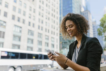 Smiling Afro businesswoman using smart phone in city - BOYF01943