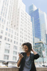 Afro female entrepreneur using smart phone in front of office buildings in city - BOYF01948