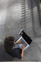 Berufstätige Frau, die im Freien sitzend einen Laptop benutzt - BOYF01956