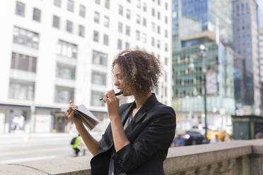 Female entrepreneur reading diary while standing near office buildings in city - BOYF01958