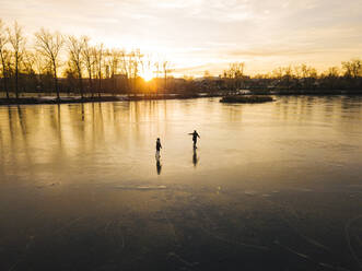 Freunde beim Schlittschuhlaufen auf einem zugefrorenen Teich bei Sonnenuntergang - KNTF06185