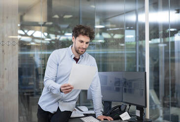 Male entrepreneur looking at strategy while leaning on desk at factory - FKF04014