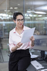 Smiling businesswoman with strategy sitting at desk in office - FKF04017