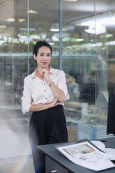 Geschäftsfrau lehnt an Glaswand im Büro - FKF04026