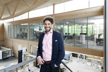 Smiling male entrepreneur leaning on railing in factory - FKF04059