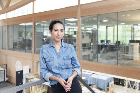 Businesswoman leaning on railing at office - FKF04065