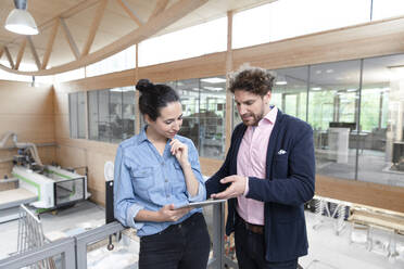 Male entrepreneur explaining strategy to female colleague over digital tablet in factory - FKF04070