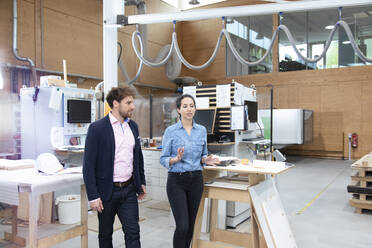 Male and female entrepreneurs discussing while walking in factory - FKF04080