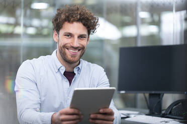 Lächelnder männlicher Unternehmer mit digitalem Tablet im Büro - FKF04104