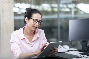 Unternehmerin, die ein digitales Tablet benutzt, während sie am Schreibtisch im Büro sitzt - FKF04105