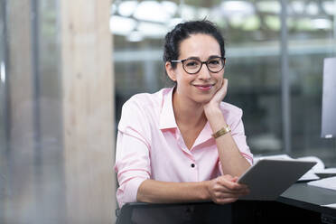 Smiling businesswoman with eyeglasses holding digital tablet at office - FKF04107