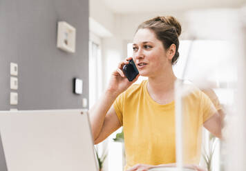 Unternehmerin, die bei der Arbeit zu Hause mit ihrem Smartphone telefoniert - UUF22895