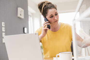 Businesswoman talking on phone while working at home - UUF22897