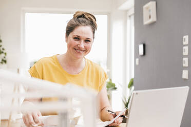 Happy female business professional working while sitting at desk - UUF22899