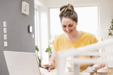 Lächelnde Geschäftsfrau, die an einem Dokument arbeitet, während sie am Schreibtisch sitzt - UUF22900