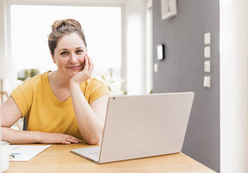 Smiling female professional sitting with laptop at desk - UUF22905